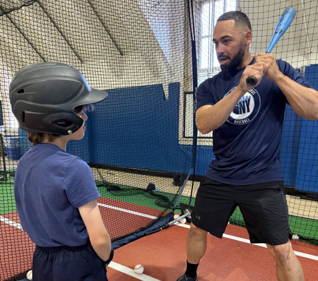 Baseball coach instructing young player indoors.
